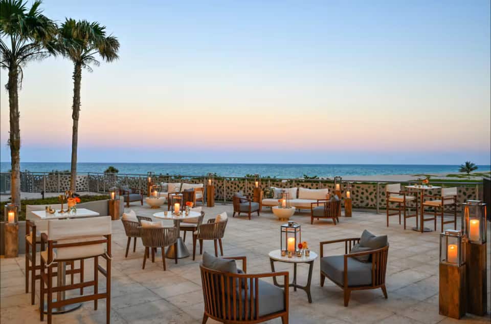 The oceanfront terrace at dusk, with lantern-lit tables under palms