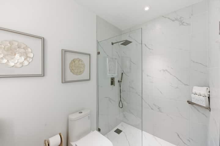 The second bathroom's marble walk-in shower behind glass, with framed shell artwork