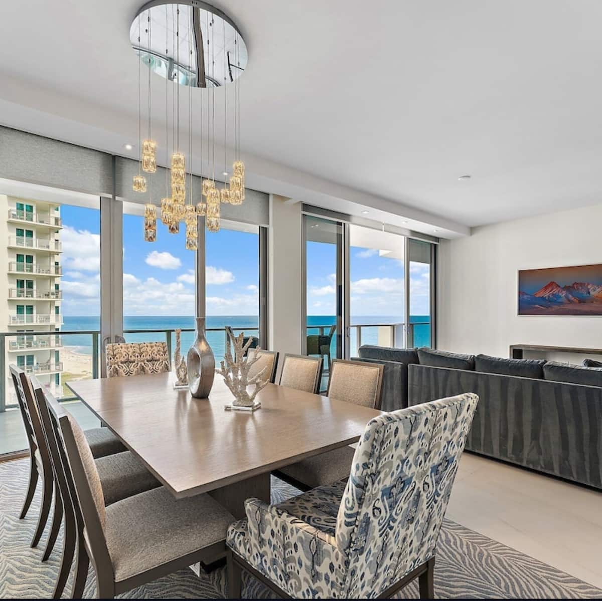The dining table for eight beneath a glass chandelier, ocean beyond