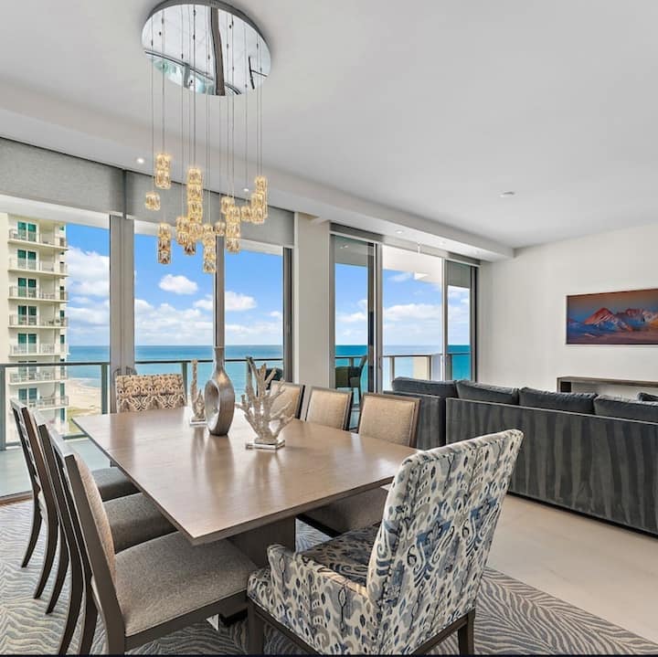 The dining table for eight beneath a glass chandelier, ocean beyond
