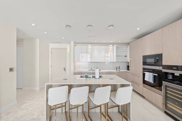 The open kitchen with a long island, four bar stools, a wine fridge and a cluster of pendant lights