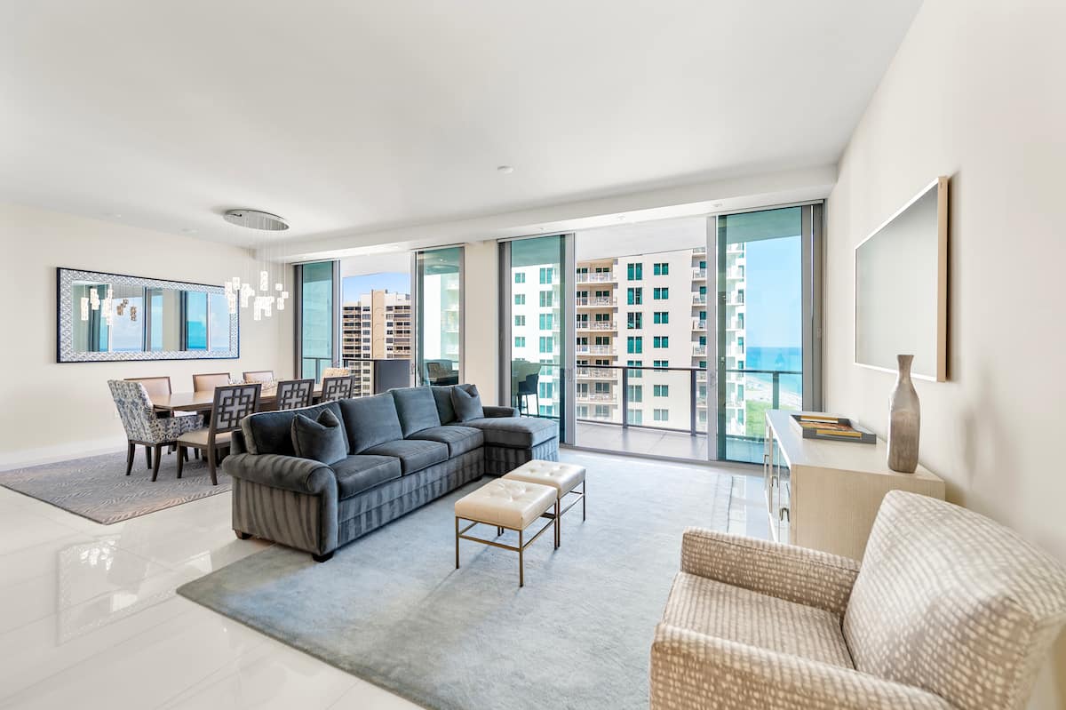 The open living and dining room wrapped in glass on two sides, with a sectional sofa facing the ocean