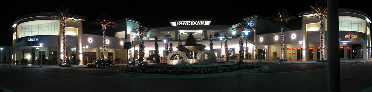 The main entrance of Downtown at the Gardens in Palm Beach Gardens lit up at night, with palms and a fountain