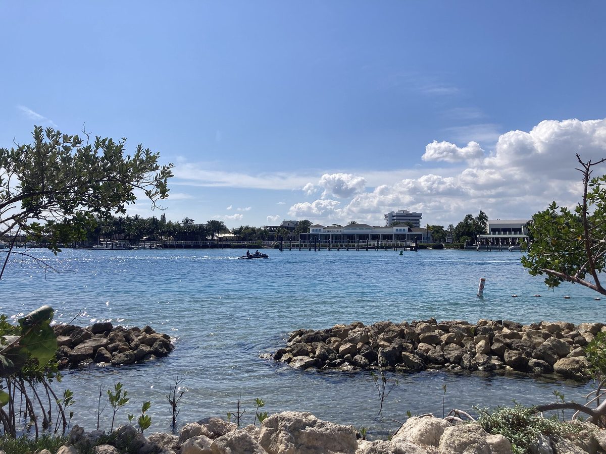 Blue water of the Jupiter Inlet seen from the nature trail at the Jupiter Inlet Lighthouse, with a boat crossing and waterfront buildings beyond