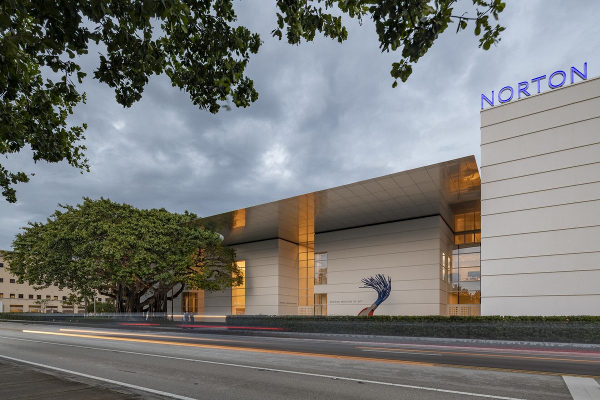 The Foster + Partners front of the Norton Museum of Art at dusk, with its large canopy and a banyan tree beside the entrance