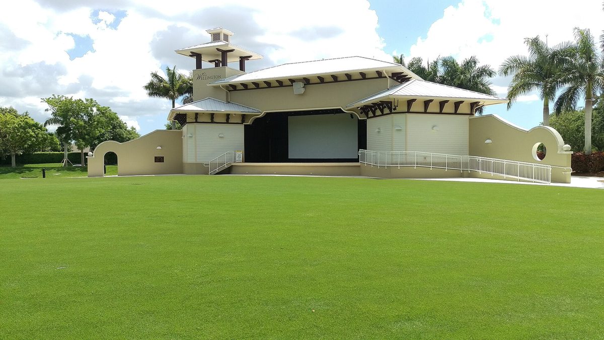 The Wellington Amphitheater stage and its lawn at the town center in Wellington, Florida, under a blue sky with palms